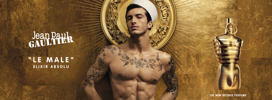 Jean Paul Gaultier Le Male Elixir Absolu Werbekampagne mit einem muskulösen, tätowierten Mann in Matrosenmütze vor goldener Aura, neben dem glänzenden, goldenen Parfumflakon.