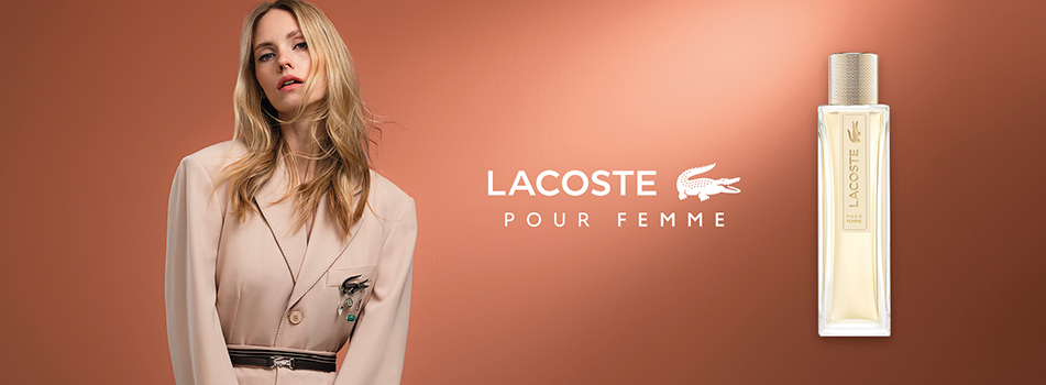 Werbebanner für das Damenparfum Lacoste Pour Femme: Eine Frau in beigefarbener, eleganter Kleidung steht vor einem warmen braunen Hintergrund, rechts daneben steht der schlichte, rechteckige Flakon des Parfums mit goldenem Verschluss und der Aufschrift „Lacoste Pour Femme“.