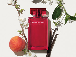 Roter Parfumflakon von 'narciso rodriguez for her' liegt auf hellem Untergrund. Umgeben ist er von frischen weißen Blüten, grünen Blättern, einer Pfirsichfrucht und zwei Vanilleschoten – symbolisch für die Duftnoten des Parfums.