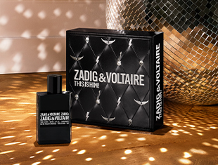 Schwarzes Parfumset Zadig & Voltaire This Is Him! auf gold schimmernder Fläche mit Lichtreflexen einer Diskokugel. Links steht der schwarze Flakon, rechts die passende Geschenkbox mit gepolstertem Lederdesign und silbernen Nieten.